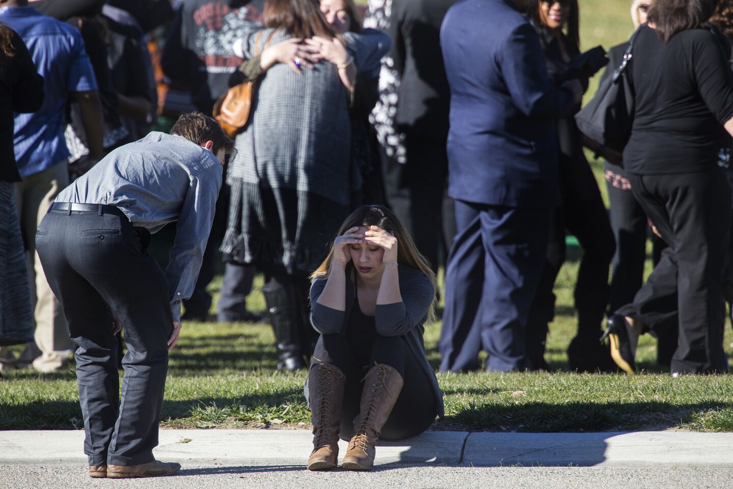 A mourner sits on the curb with her head in her hands during the graveside ceremony for San Bernardino shooting victim Robert Adams at Montecito Memorial Park in Colton.