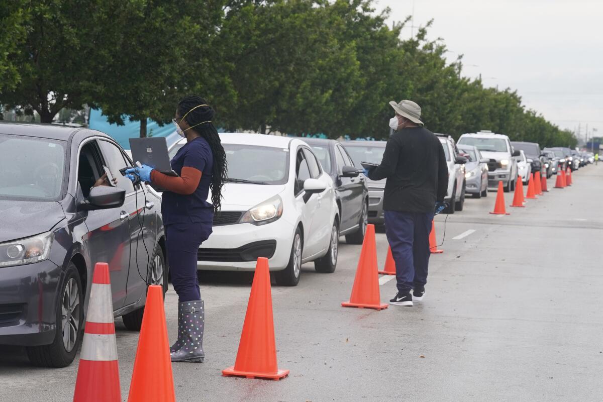 Nomi Health workers check in a long line of people for coronavirus tests in North Miami, Fla.