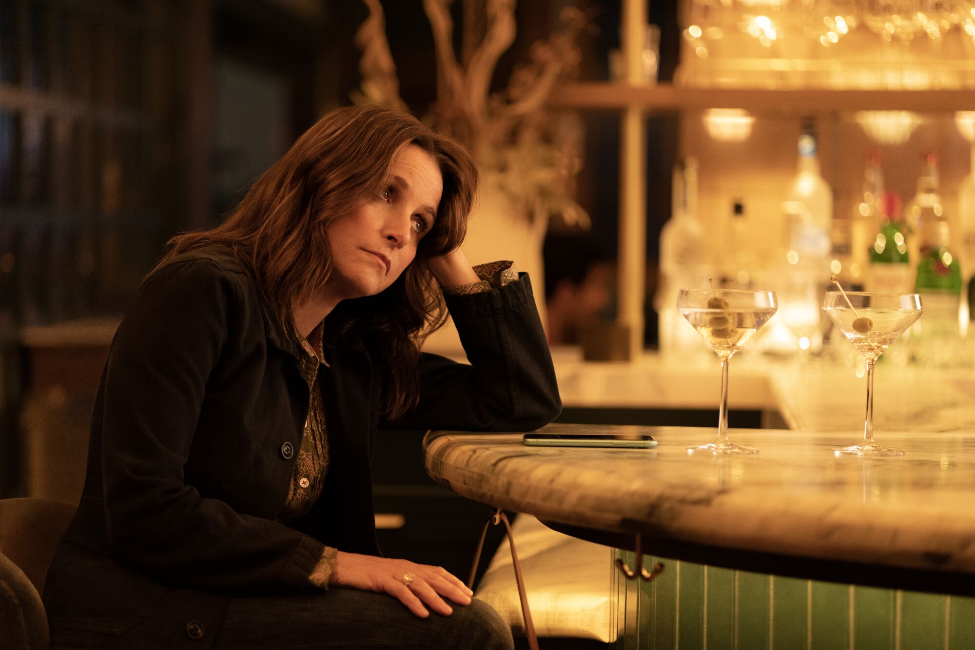 A woman leans on her arm at a bar, looking forlorn.