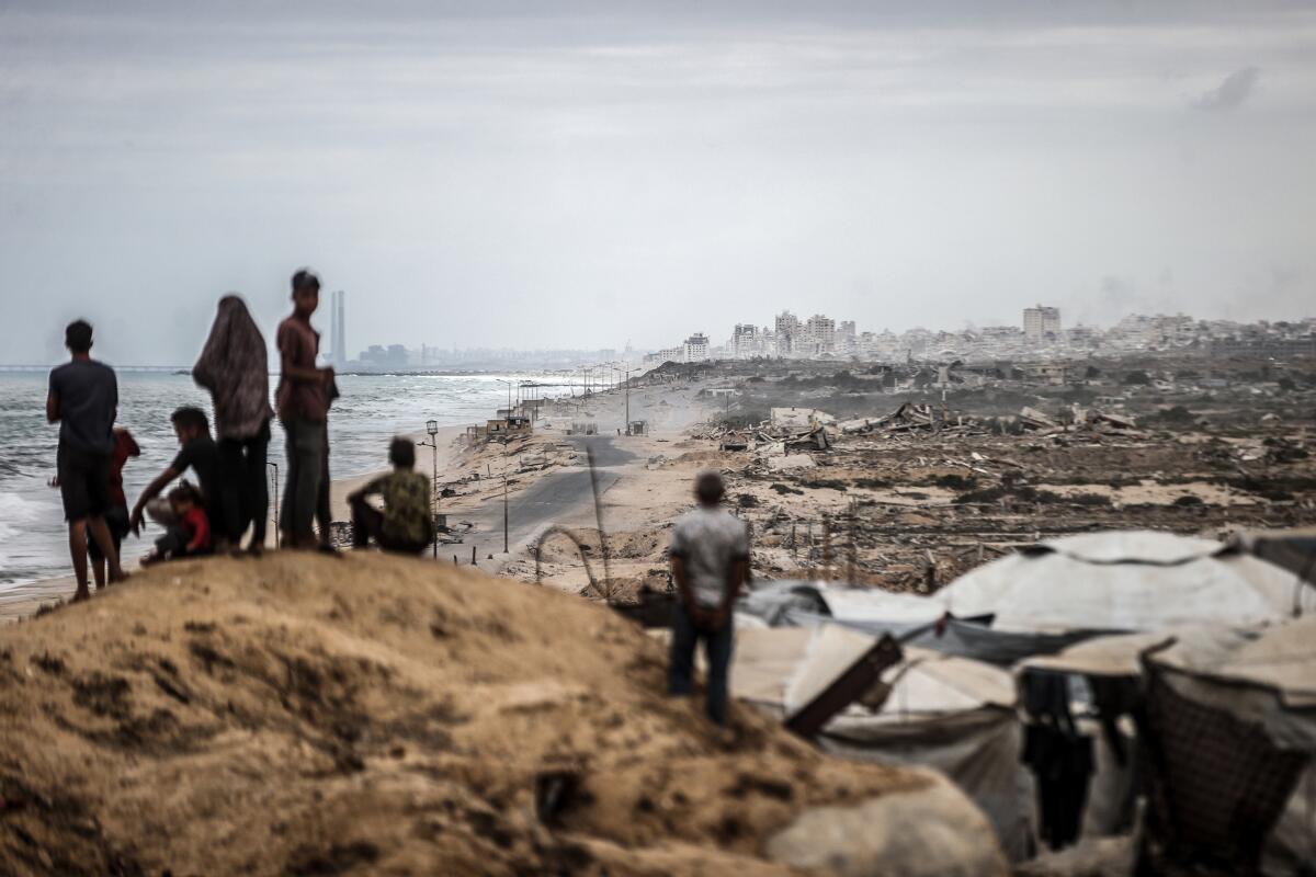 People standing on a hill with a view of the ocean, overlooking tents