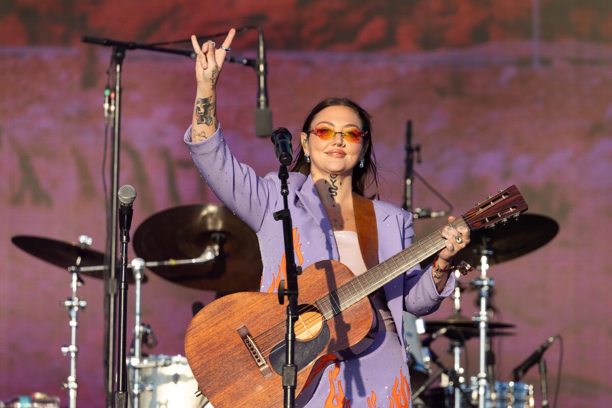 Une guitariste lève la main droite dans le symbole des cornes de rock pendant qu'elle joue.