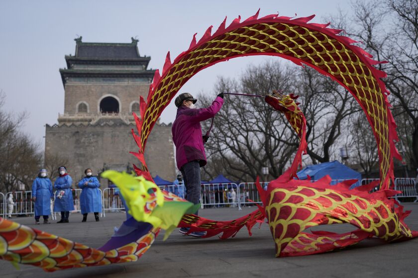 Community workers wearing protective suits watch over a masked resident twirling a dragon shaped ribbon near a barricaded coronavirus testing site setup outside the Drum Tower, Wednesday, March 23, 2022, in Beijing, China. A fast-spreading variant known as "stealth omicron" is testing China's zero-tolerance strategy, which had kept the virus at bay since the deadly initial outbreak in the city of Wuhan in early 2020. (AP Photo/Andy Wong)