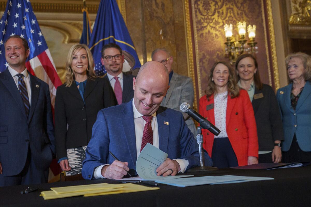 Utah Gov. Spencer Cox signs two social media regulation bills as people stand behind him. 