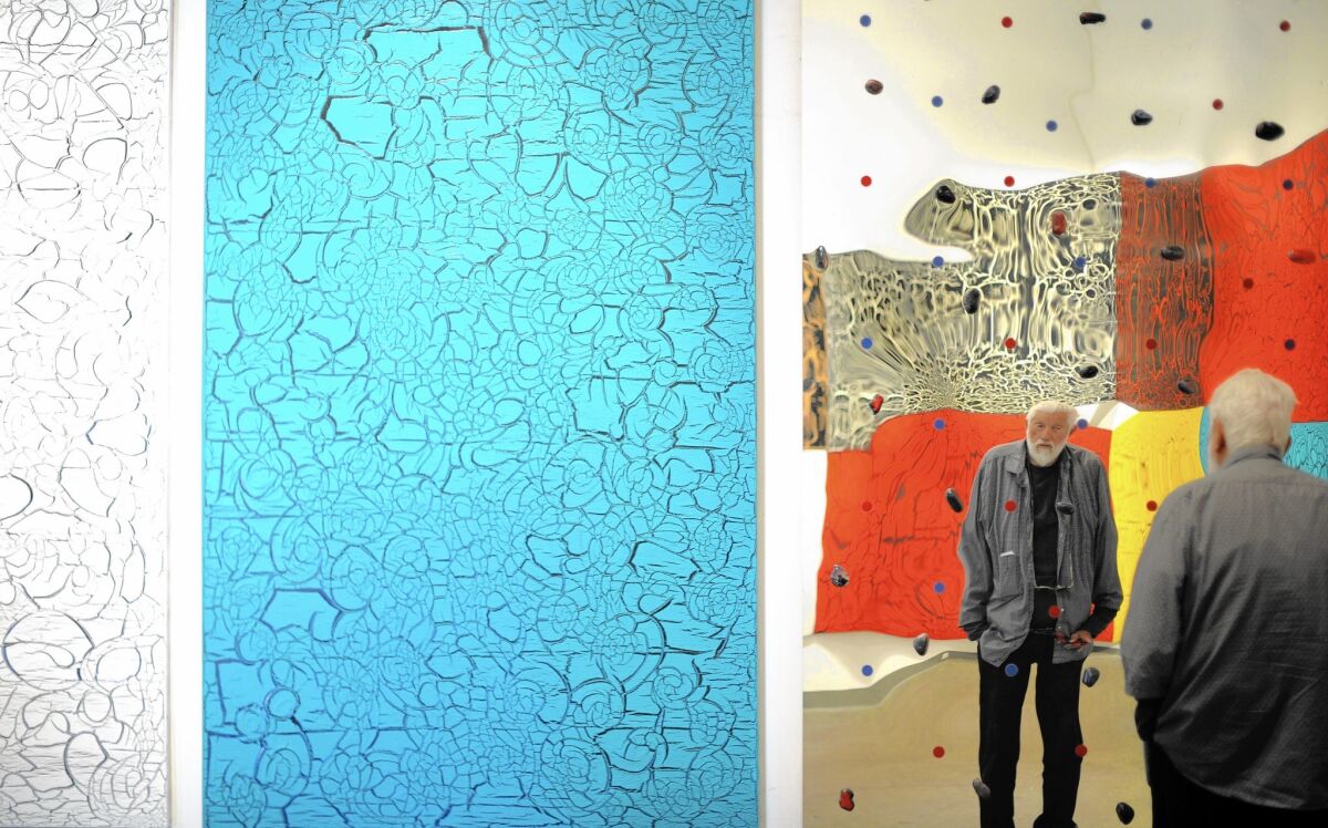 Artist Ed Moses is reflected in the aluminum surface of a work studded with painted rocks before a survey exhibition at William Turner Gallery on Saturday.