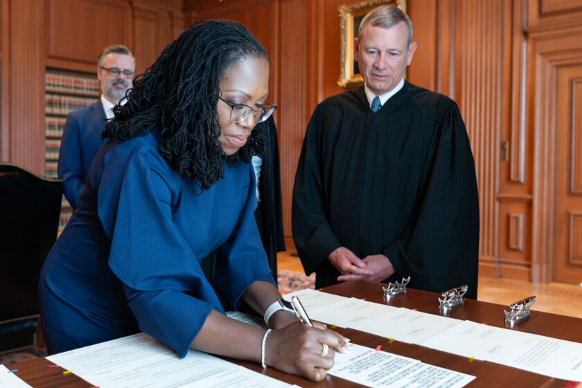 Chief Justice John G. Roberts, Jr., looks on as Justice Ketanji Brown Jackson signs the Oaths of Office