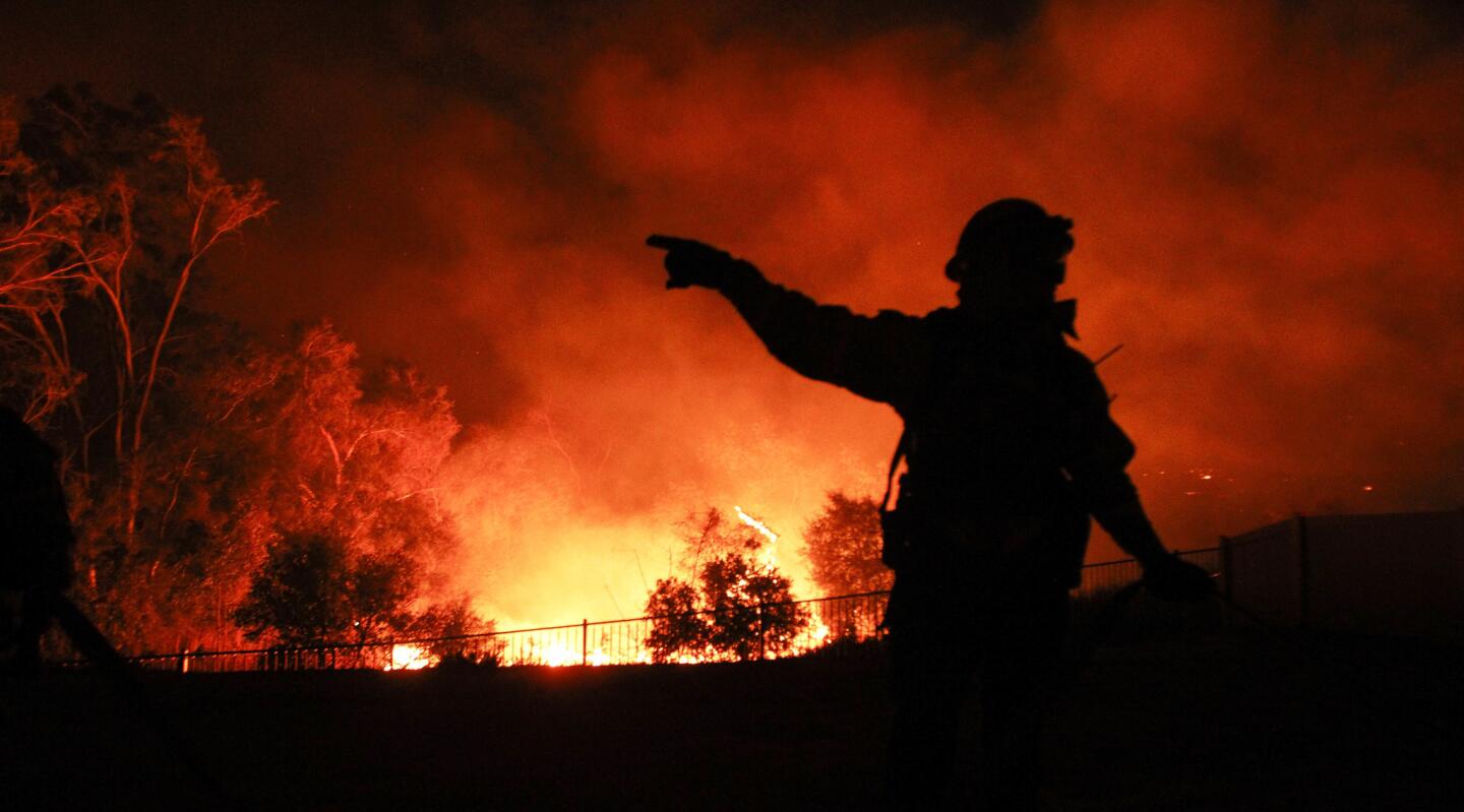 A San Diego Fire and Rescue firefighters gestures while talking to another firefighter as they protect a home from the Lilac Fire in Bonsall.