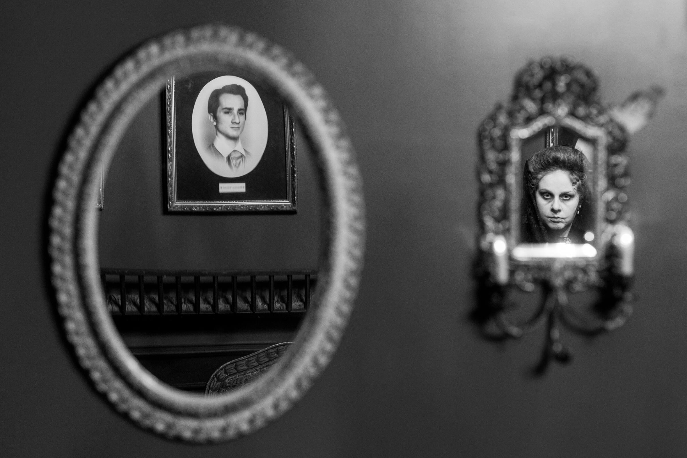 A reflection in a mirror of a portrait hung on the wall, left, and the character Dolores, played by Emma Kuhn.