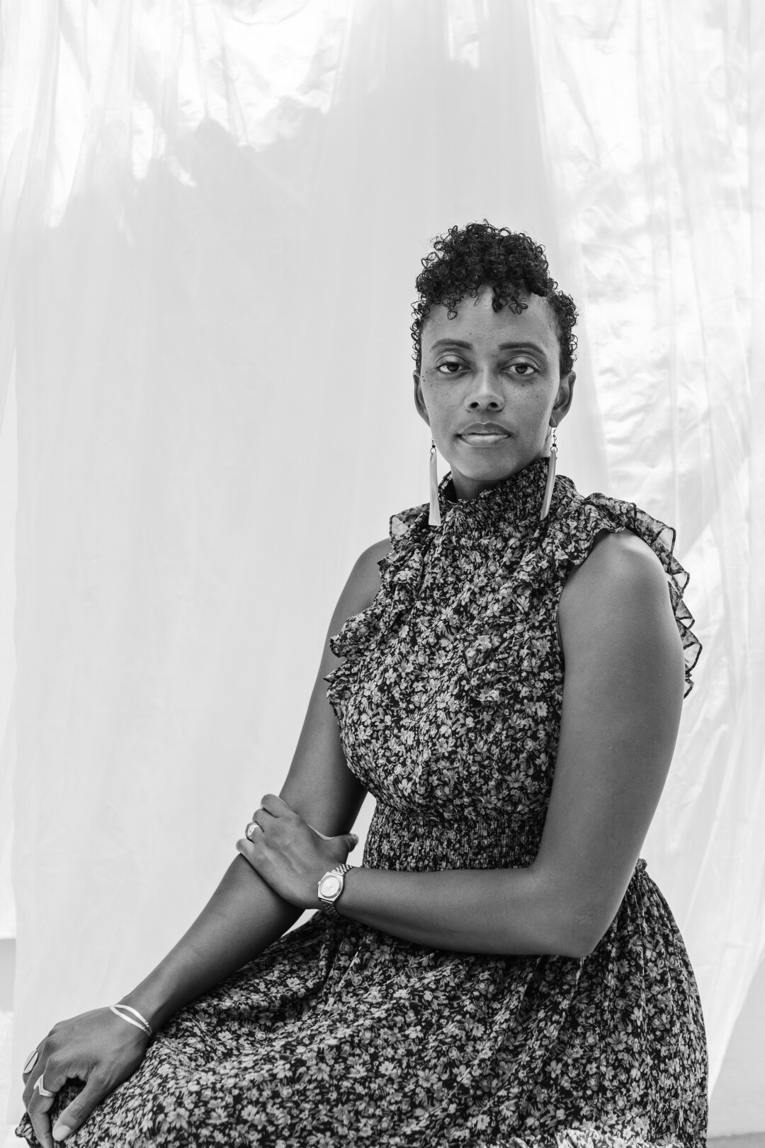 A black and white portrait of writer Angela Flournoy wearing a floral dress sitting in front of a fabric backdrop