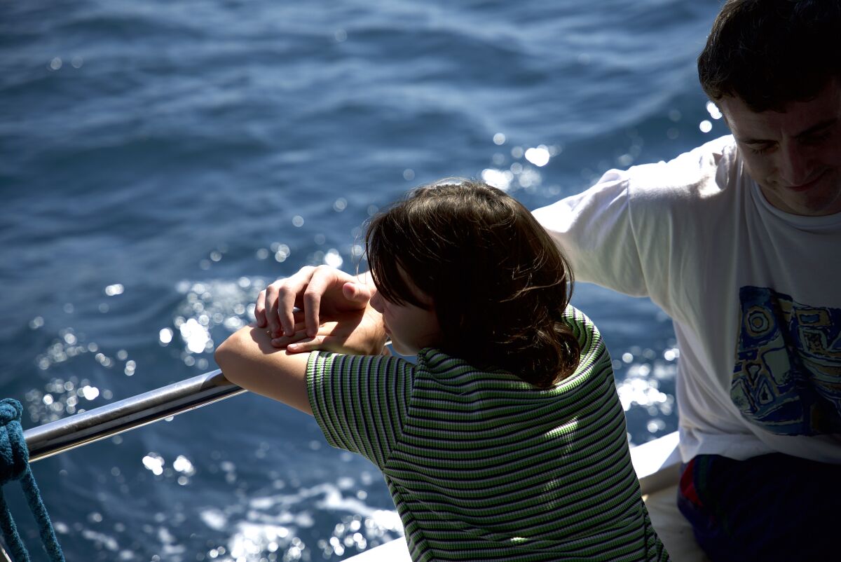 A girl leans against the edge of a boat and rests on her father's arm 