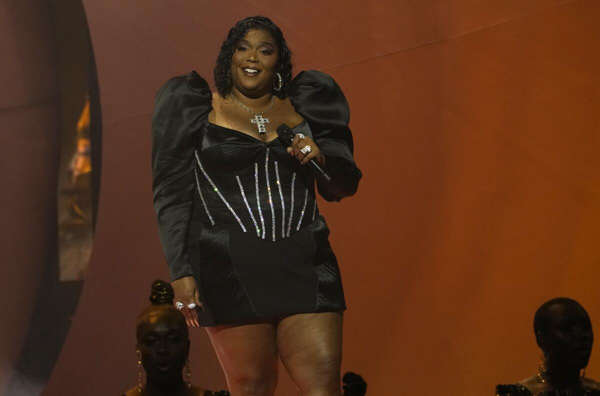 Lizzo wears a black dress and holds a microphone onstage.