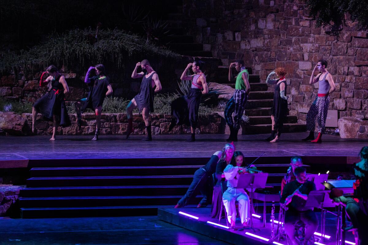 Dancers stand in a line on the stage above musicians.