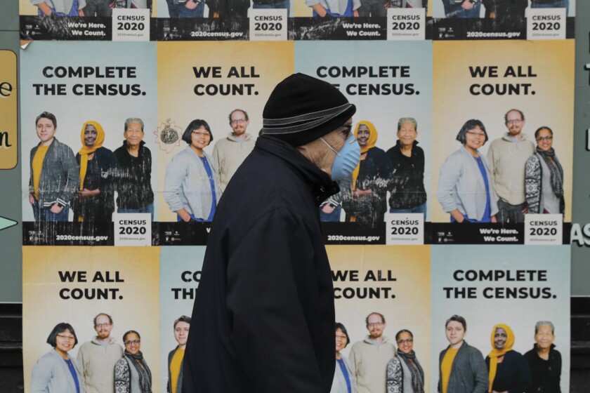 A man wearing a mask walks past posters encouraging participation in the 2020 Census, Wednesday, April 1, 2020, in Seattle's Capitol Hill neighborhood. (AP Photo/Ted S. Warren)