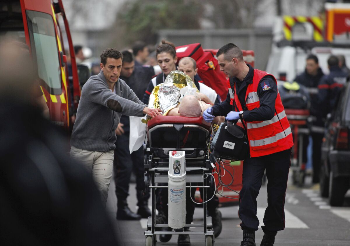 FILE - In this Jan. 7, 2015 file photo, an injured person is transported to an ambulance after a shooting at the French satirical newspaper Charlie Hebdo's office, in Paris. The January 2015 attacks against Charlie Hebdo and, two days later, a kosher supermarket, touched off a wave of killings claimed by the Islamic State group across Europe. Seventeen people died along with the three attackers. Thirteen men and a woman accused of providing the attackers with weapons and logistics go on trial on terrorism charges Wednesday Sept. 2, 2020. (AP Photo/Thibault Camus, File)