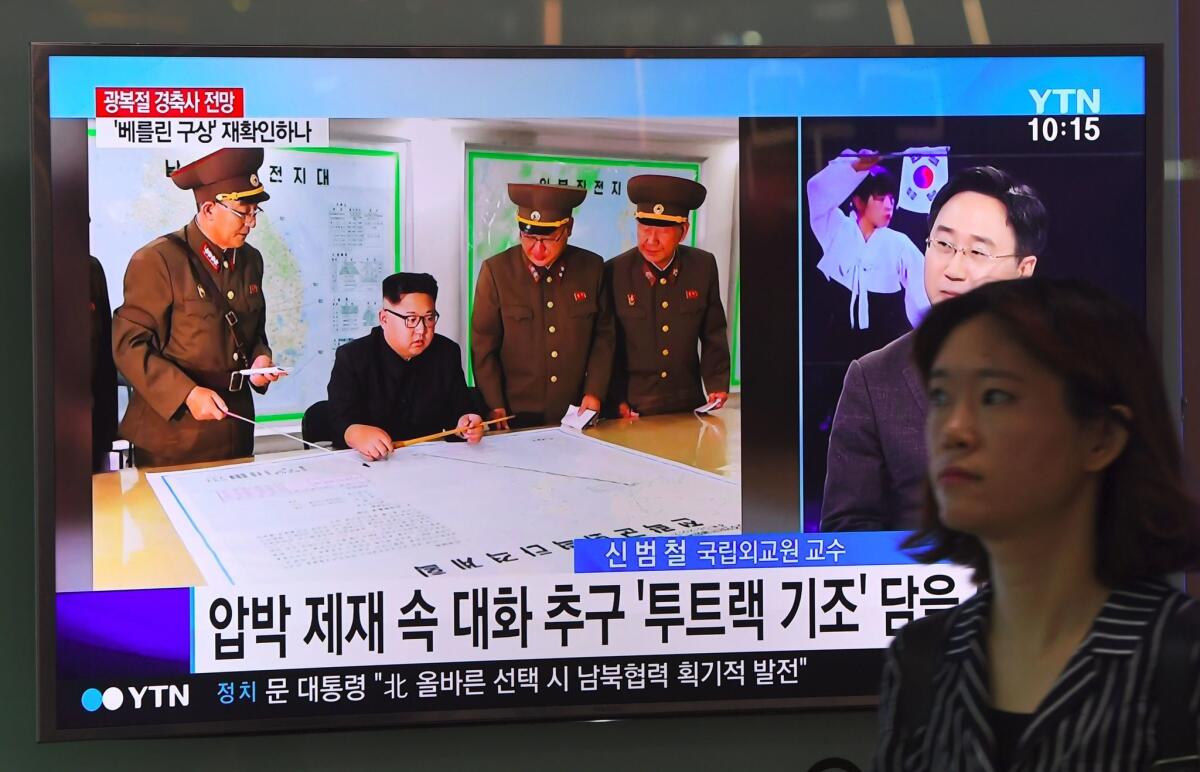 A woman walks past a television news screen showing North Korean leader Kim Jong-Un receiving a briefing, at a railway station in Seoul on August 15, 2017.
