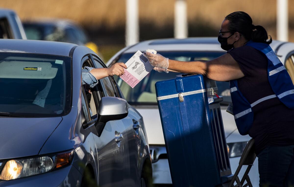 A voter hands her ballot to an election official at a drive-through ballot dropoff in Riverside.