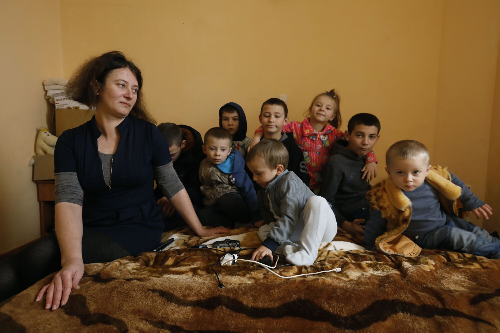 Mère avec ses huit enfants assis sur un lit dans une chambre.