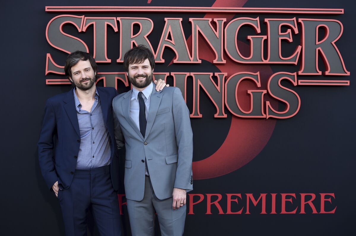 Twin brothers in suits stand in front of a Stranger Things sign