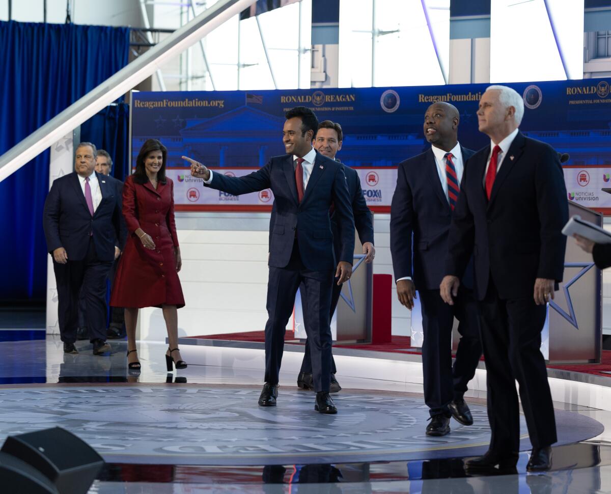 A few candidates looking into the audience as others join them on a stage decorated in red, white and blue