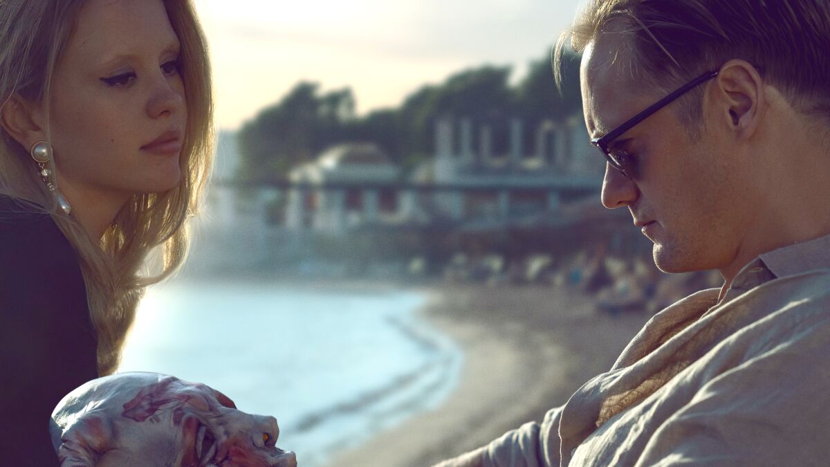 Mia Goth and Alexander Skarsgård sit outdoors in 'Infinity Pool.'