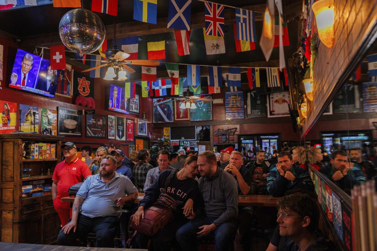 A crowd of people watch the presidential debate on TVs in an English pub in San Francisco