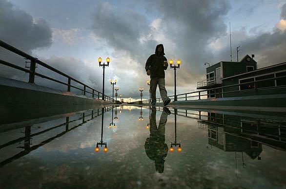 Ryan Ruppert walks along a rain-soaked Seal Beach Pier with his morning coffee. Although Southern California is wet from rain and the mountains are blanketed in snow after a series of midwinter storms, sunshine is on its way later this week, the National Weather Service says.