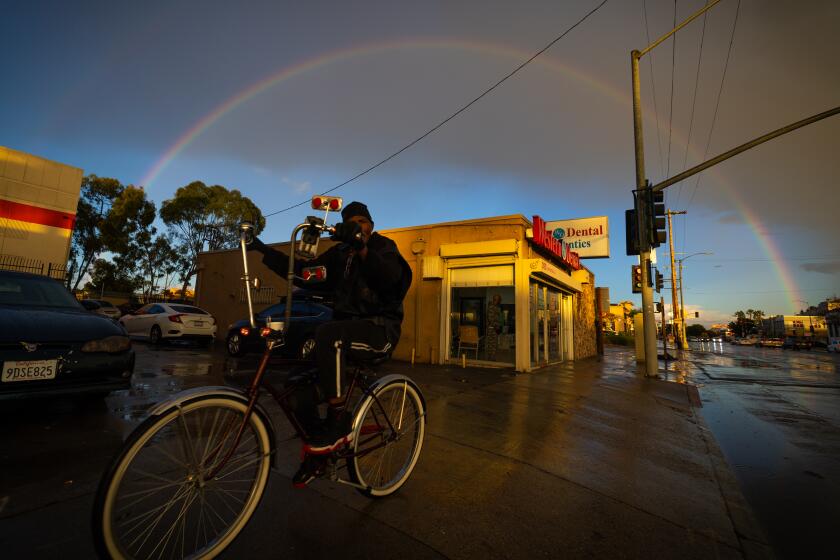 Los Angeles, CA - January 03: A man rides his bike along Manchester Ave. amid rain as a double rainbow forms and a winter storm moves into Southern California in Los Angeles Wednesday, Jan. 3, 2024. (Allen J. Schaben / Los Angeles Times)