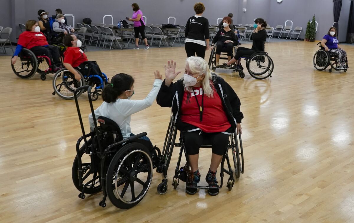 A girl and an older woman seated in wheelchairs do high-fives. 