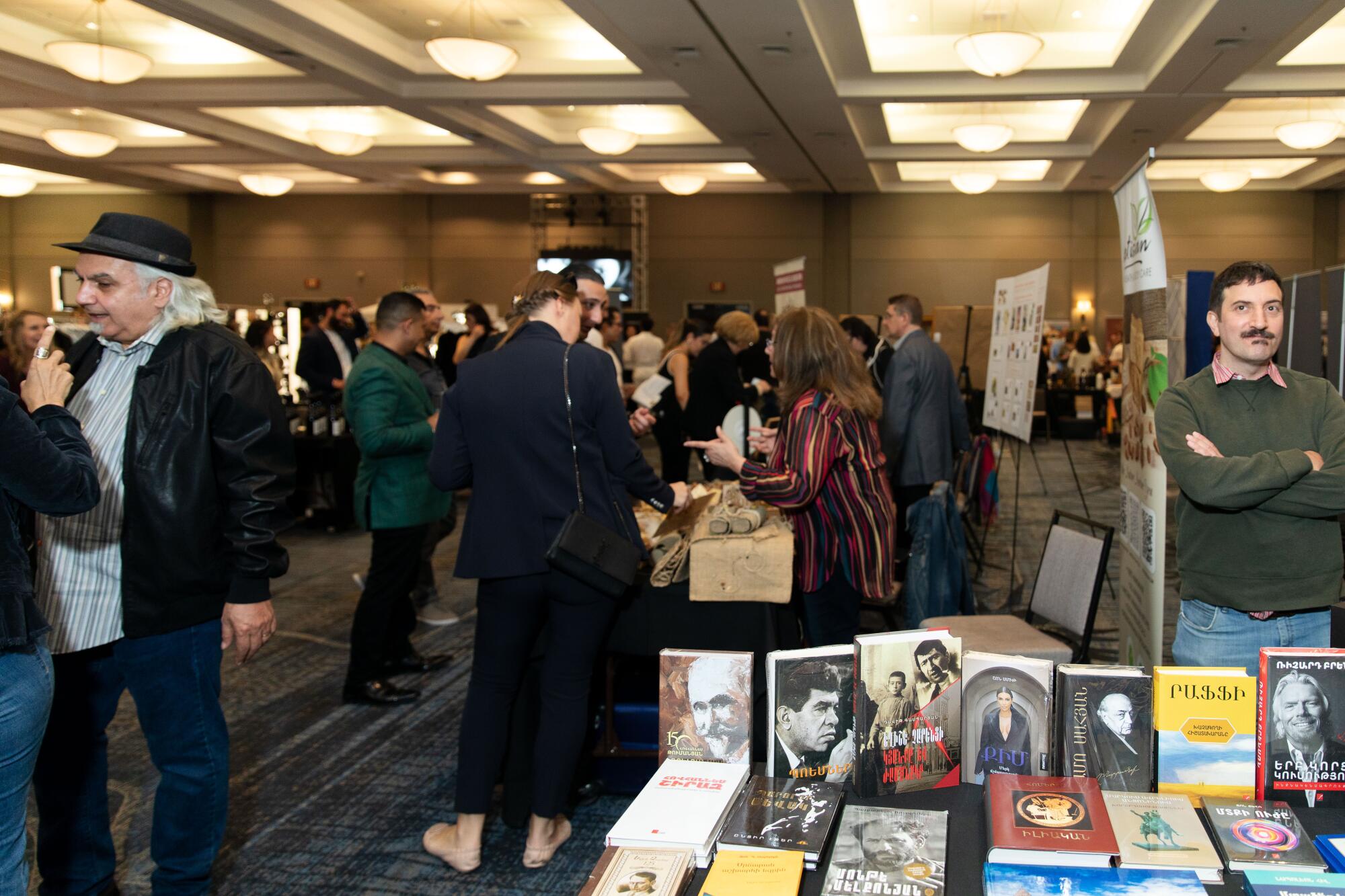 People stand in a room where tables display books and bottles of wine