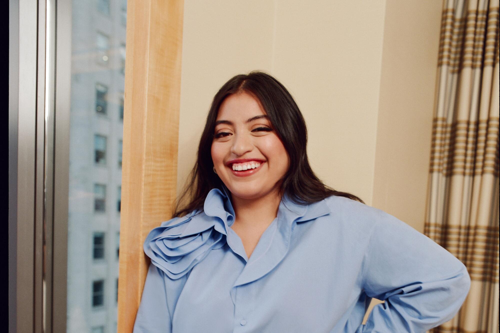 Keyla Monterroso Mejia stans smiling, in an orange skirt and light blue blouse
