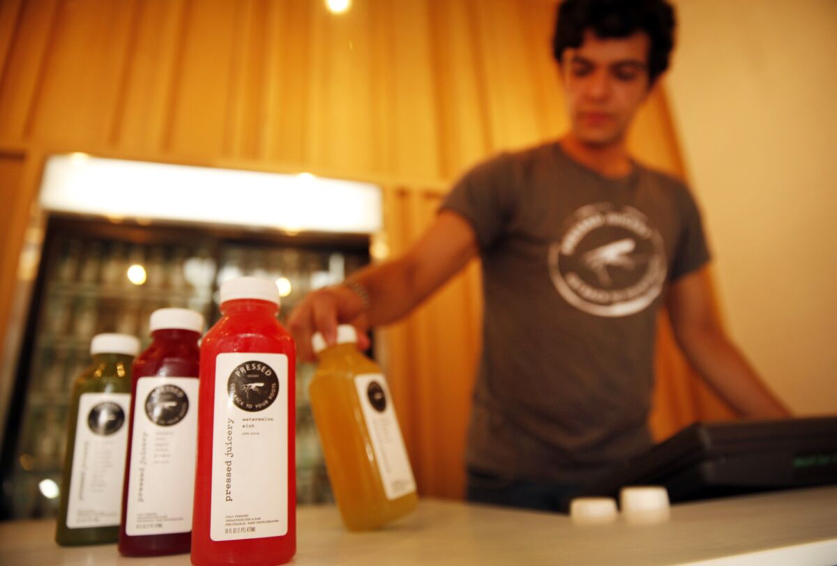 An employee at Pressed Juicery with a selection of juices from one of their refrigerated cases in the store.