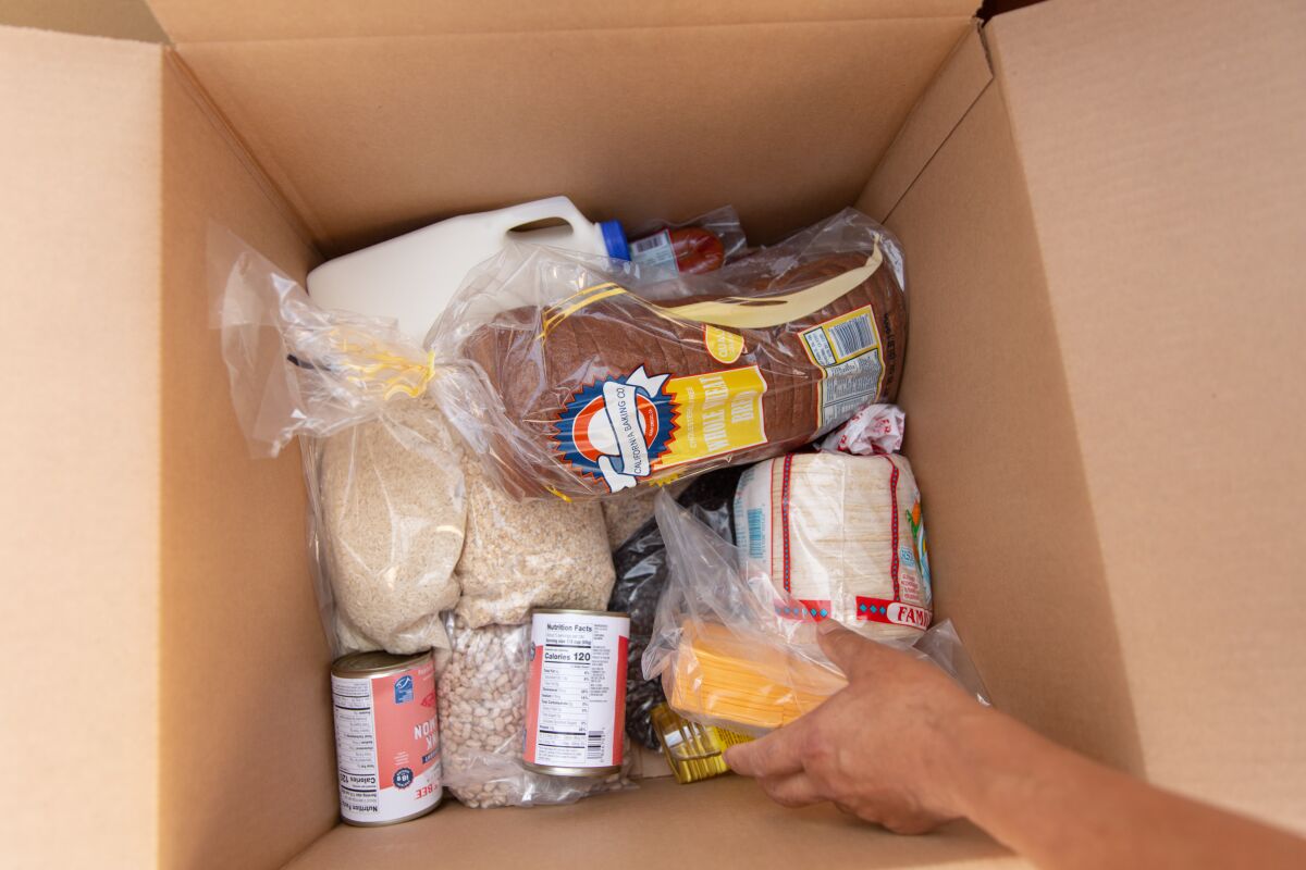 Closeup of a cardboard box as a person places a package of sliced cheese among tortillas,  bread, dry beans, etc.