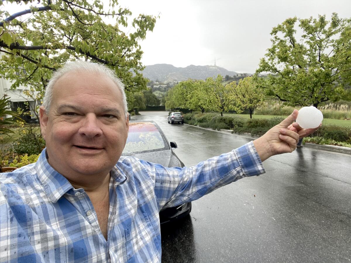 Jeff Zarrinnam takes a selfie holding a snowball with the Hollywood sign in the background.