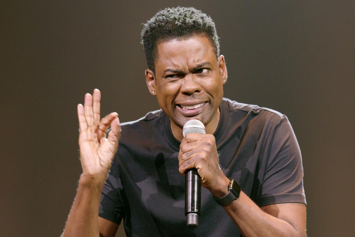 A man holding a microphone gives the OK signal with one hand while making a goofy face.