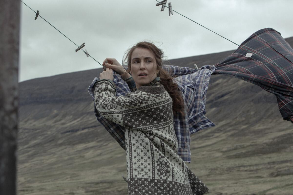 A woman in a stark landscape clips shirts to a clothesline.