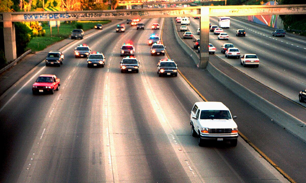 A white Ford Bronco on the freeway, trailed by numerous police cars with lights flashing