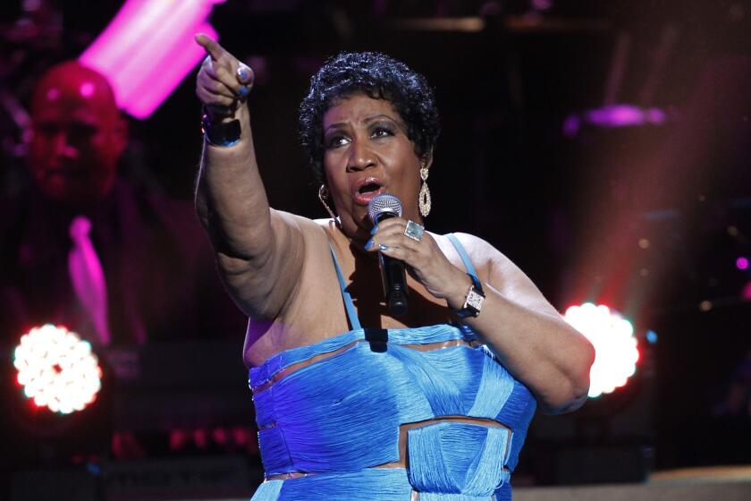 Aretha Franklin is pointing while holding a microphone to her mouth as she sings on stage, wearing a blue dress 