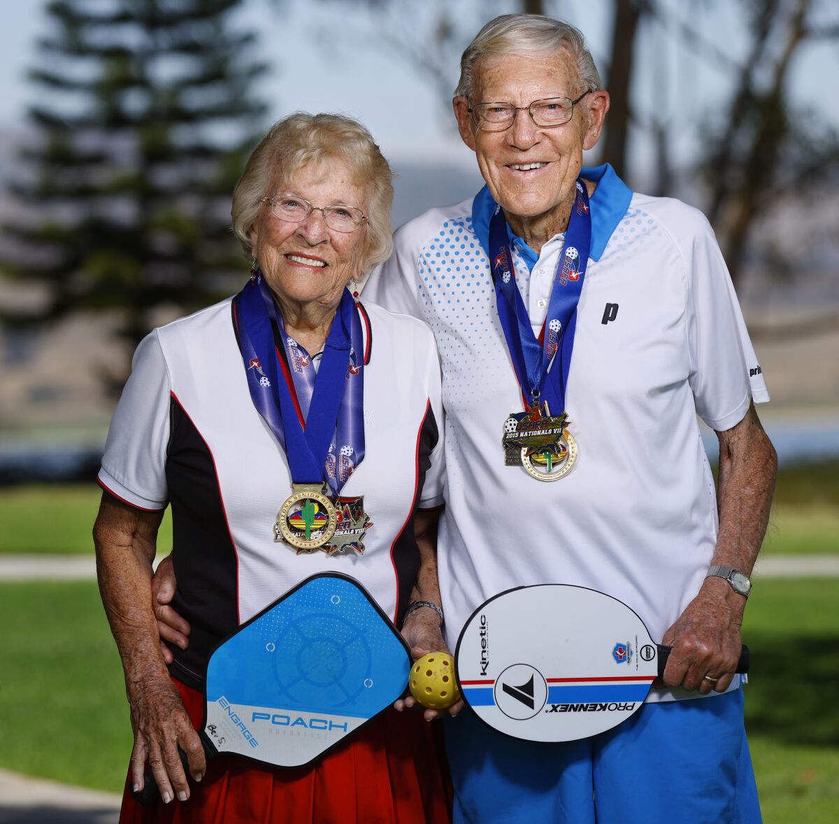 A couple wearing pickleball uniforms wearing medals and holding paddles.