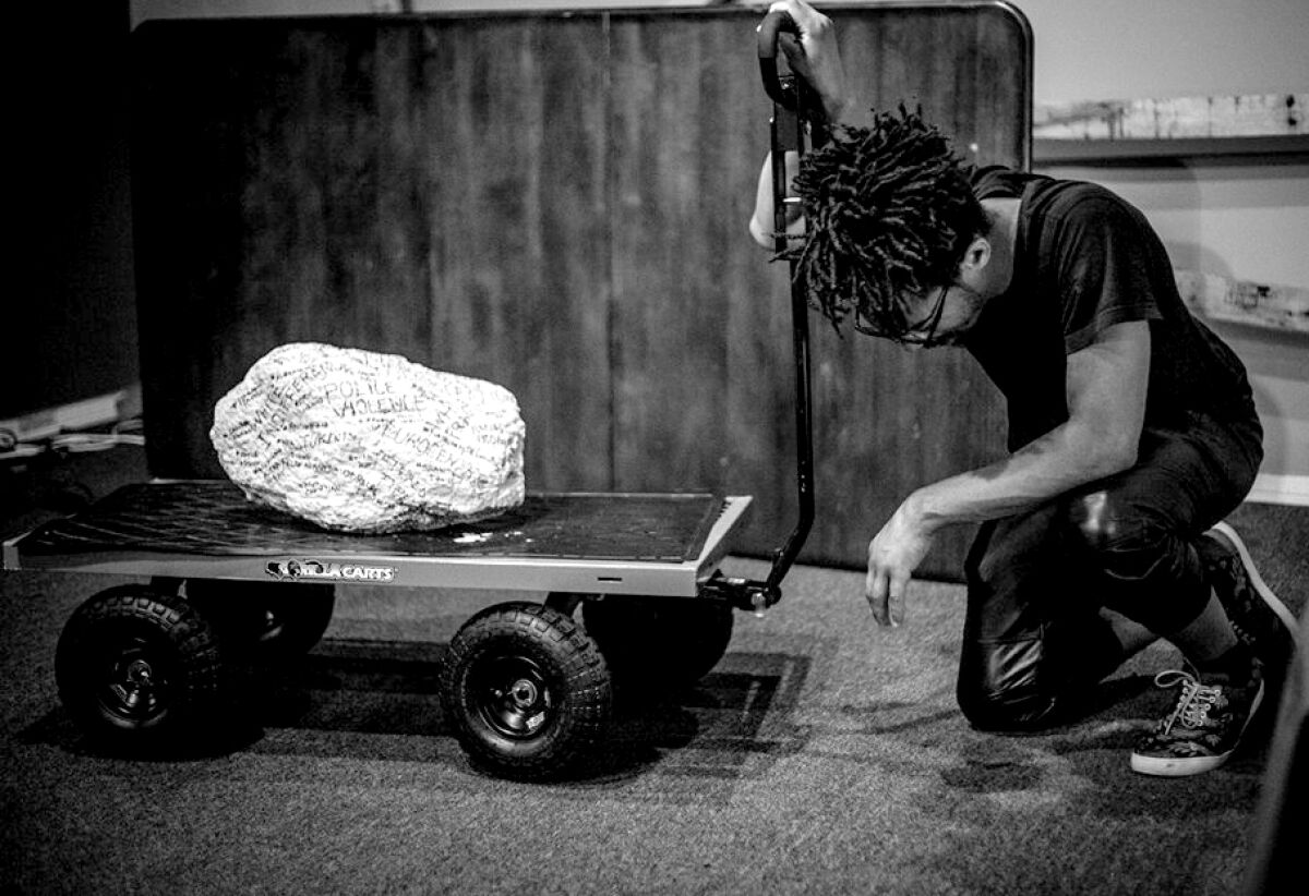 Andre Henry kneels beside a roller cart holding a chunk of rock. 