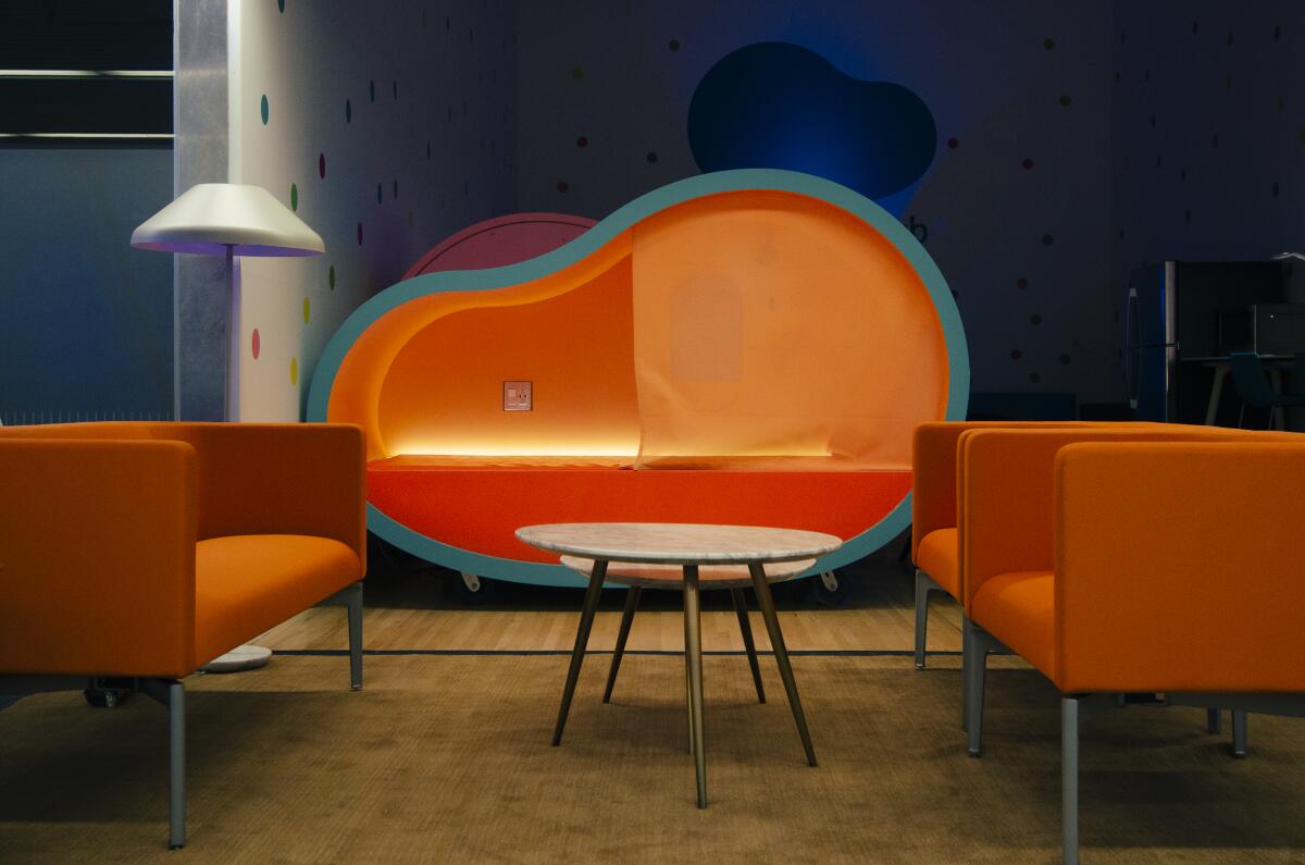 A sleeping pod, shaped like a jelly bean, glows from within. Nearby are chairs and a lamp.