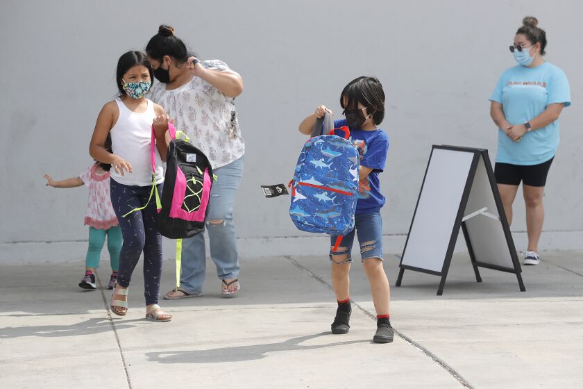Briana and Brandon Melendez, from left, walk away with new backpacks compliments of Newport-Balboa Rotary Club during distribution of back-to-school supplies from Boys and Girls Club of Central Orange County at Rea Elementary School in Costa Mesa on Friday