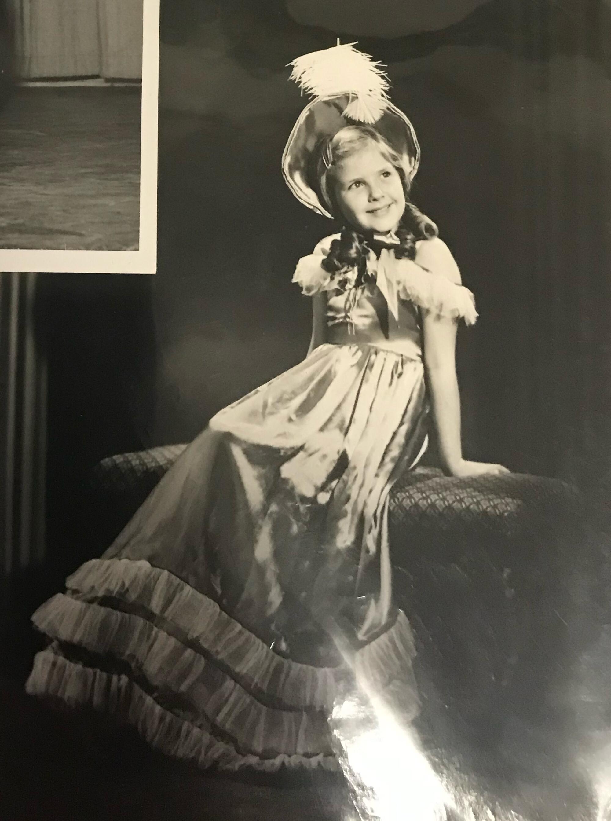 Photo of Lora Lee Michel in a dress and hat sitting on a bench.