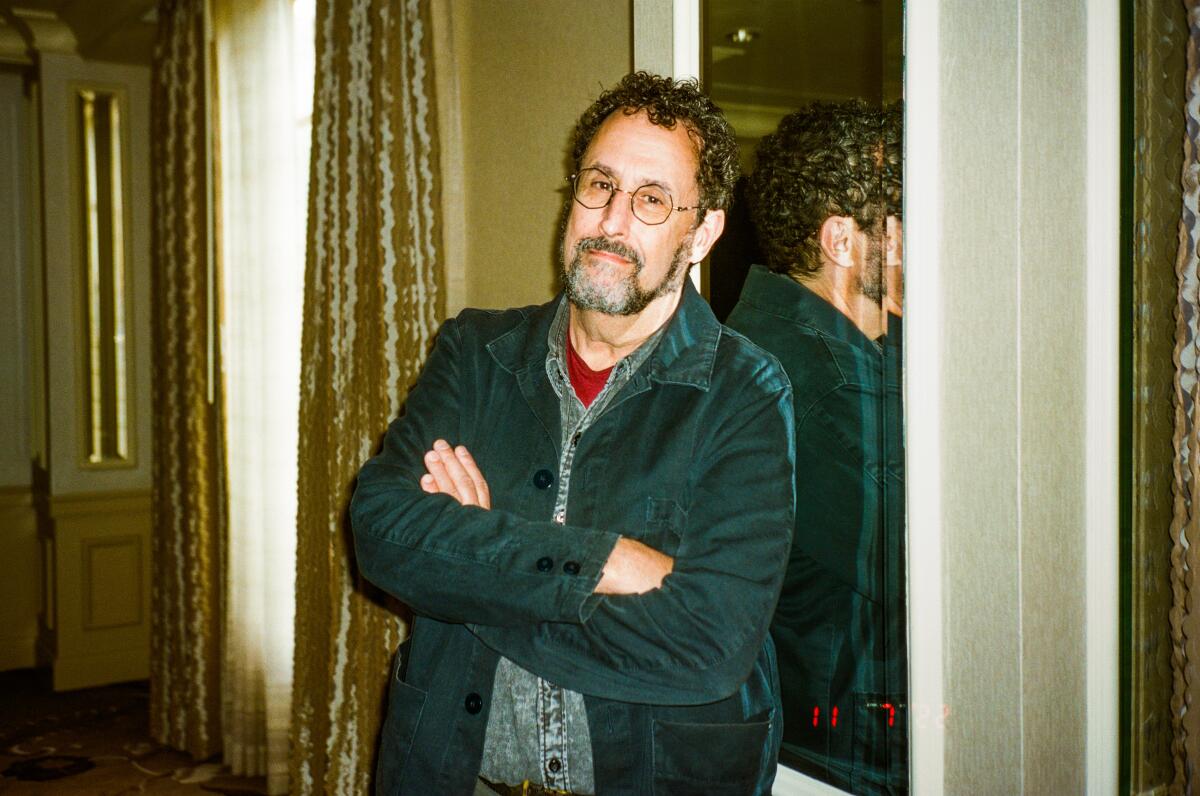 A portrait of Tony Kushner leaning back against a mirror.