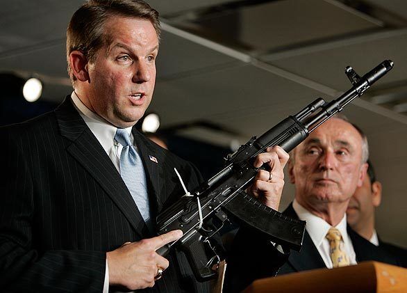 Christopher Shaefer of the Bureau of Alcohol, Tobacco, Firearms and Explosives holds an assault rifle seized during raids targeting gang members indicted for murders, drug trafficking, carjackings, home invasion robberies and witness intimation. At right is LAPD Chief William J. Bratton.