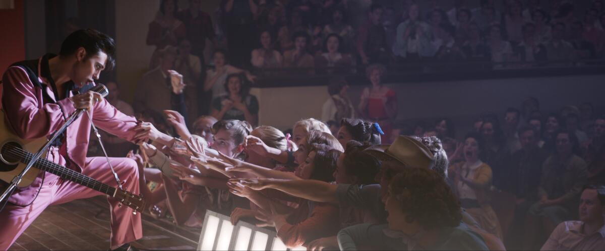 Austin Butler as Elvis Presley wears a pink suit while reaching out to fans during a performance.