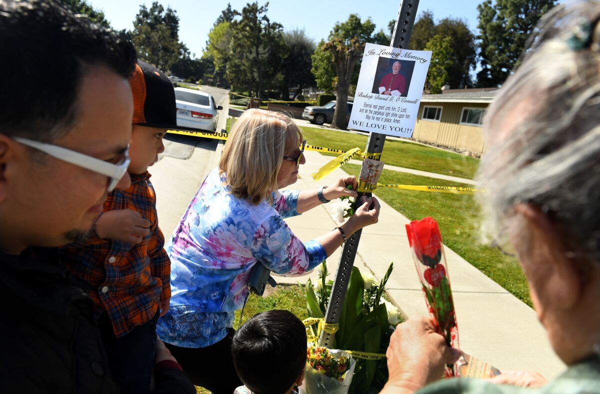 Seen through other people, a woman tapes a message to a street-sign post, while another woman holds a red flower.