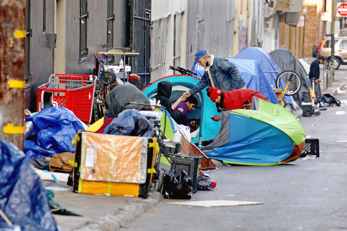 Small tents are lined up on a narrow sidewalk alongside buildings.