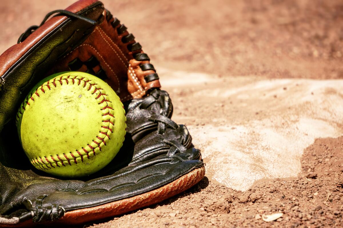 Softball in glove on dirt near a base.