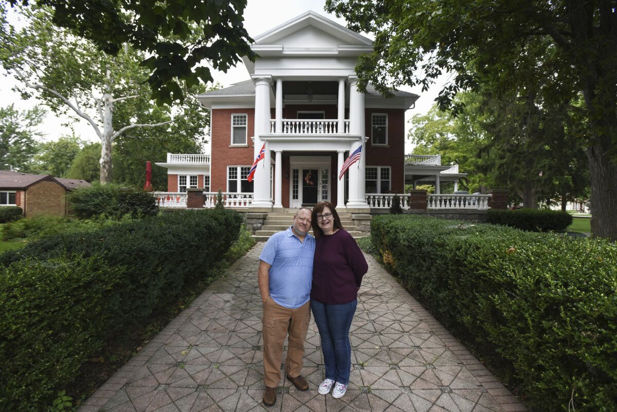 This July 2020 photo shows Kjersten and Greg Offenecker, the owners of a Civil War-era mansion turned bed and breakfast in St. Johns, Mich. The owners of the bed and breakfast have removed a Norwegian flag outside of their business after being accused of promoting racism from people who think that it is a Confederate flag. Kjersten and Greg Offenecker, owners of The Nordic Pineapple, hung the flag opposite of the American flag after they moved into the Civil War-era mansion in 2018. The red flag, with a blue cross superimposed on a white cross, is a nod to Kjersten Offenbecker’s grandfather, who was born in Norway. (Matthew Dae Smith/Lansing State Journal via AP)
