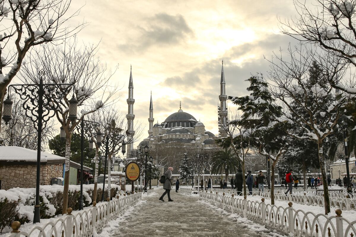 People walk in a snow-covered park with the Hagia Sophia in the background 