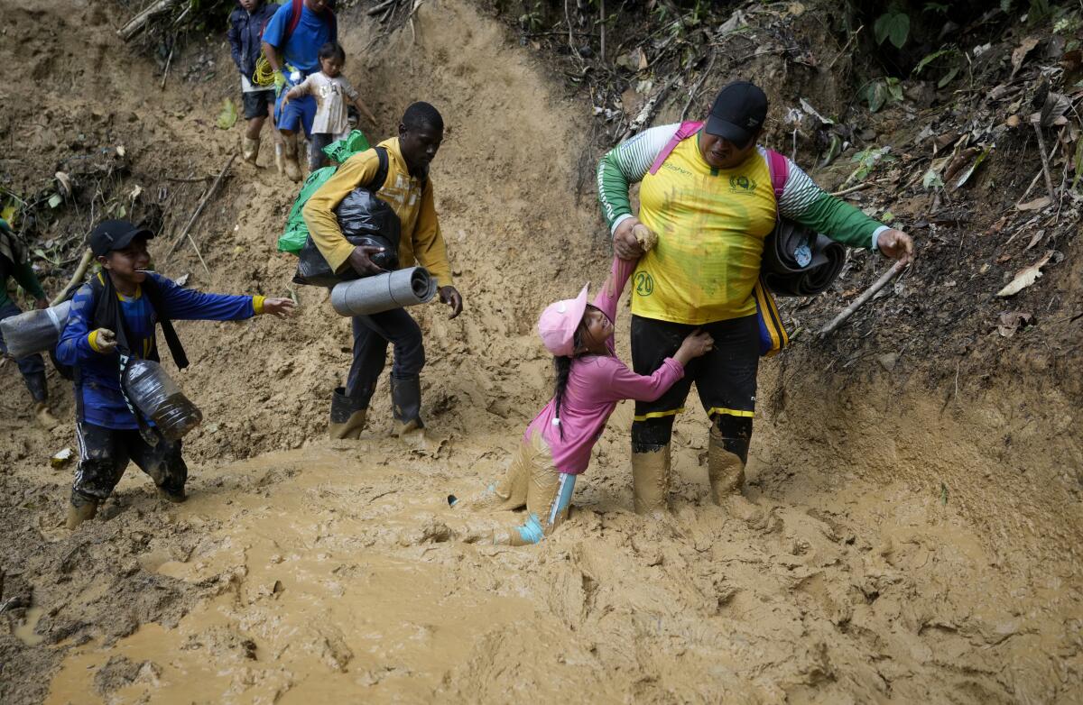 Adults and children carrying bags as they wade through mud